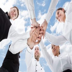 Directly below shot of chef and waiters piling hands against sky